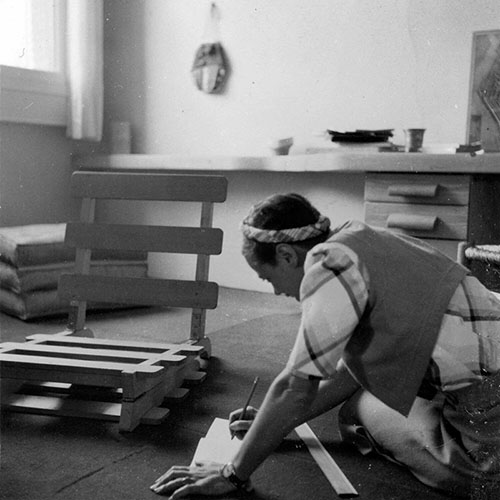Charlotte Perriand writing notes next to a chair 